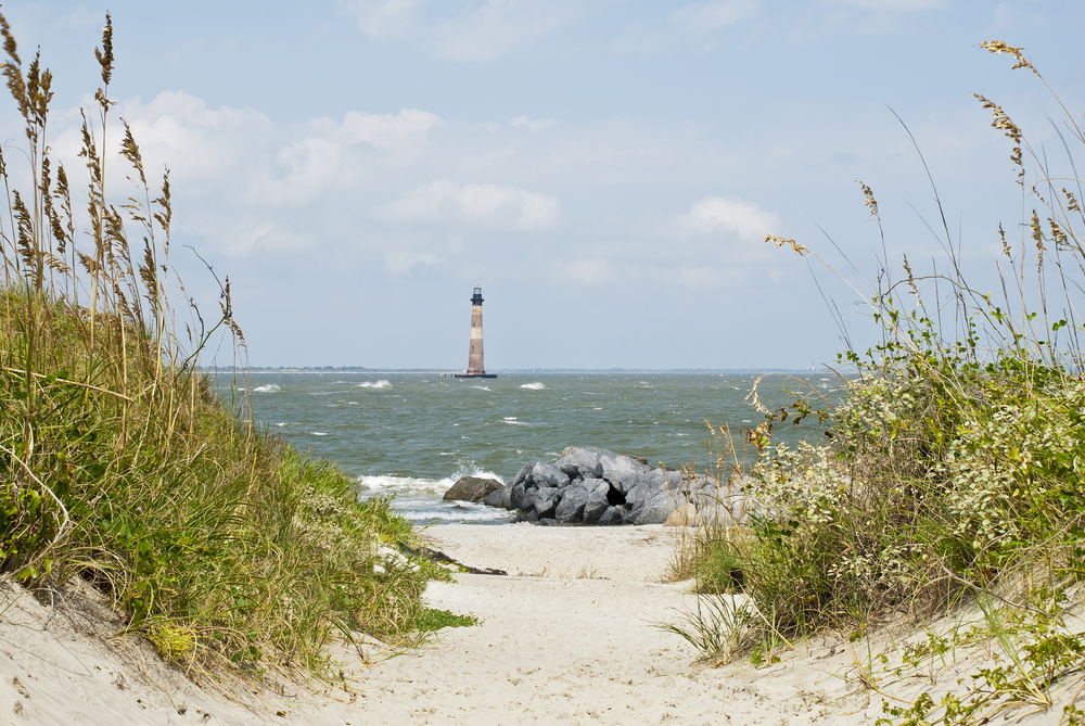 sandy path leading to water with a lighthouse in the distance