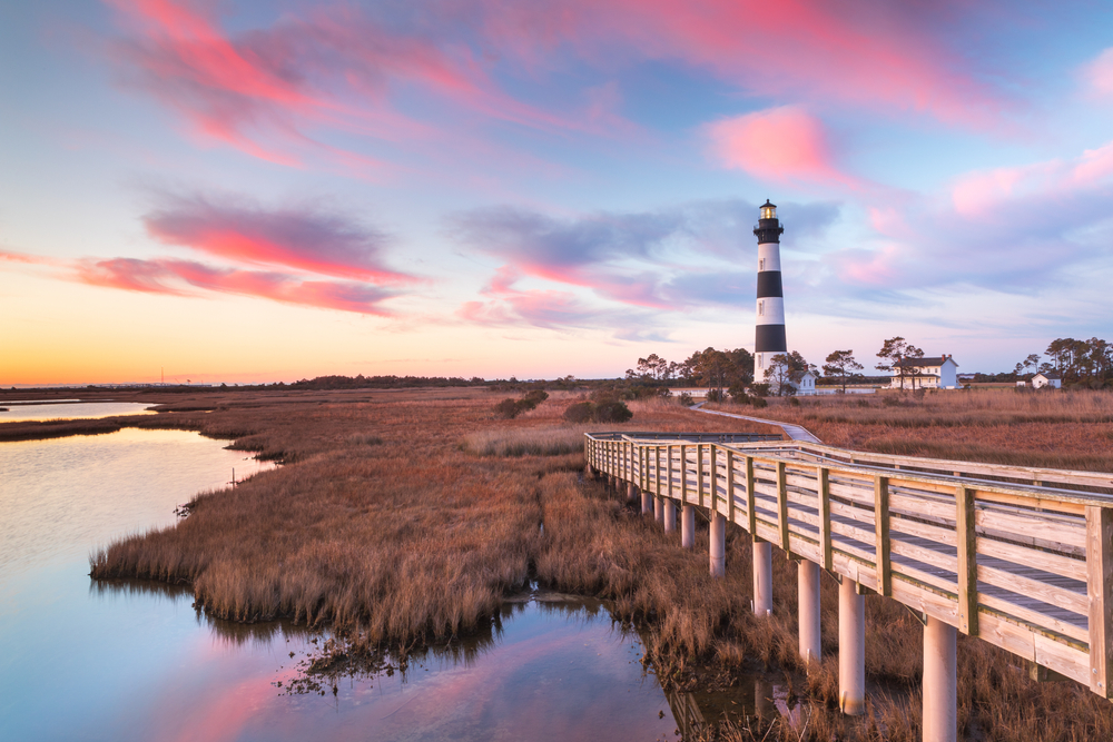 beautiful sunset over wooden boardwalk, water, and lighthouse