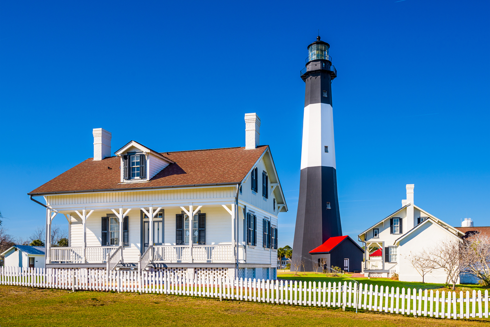 black and white striped lighthouse next to white building on a sunny day