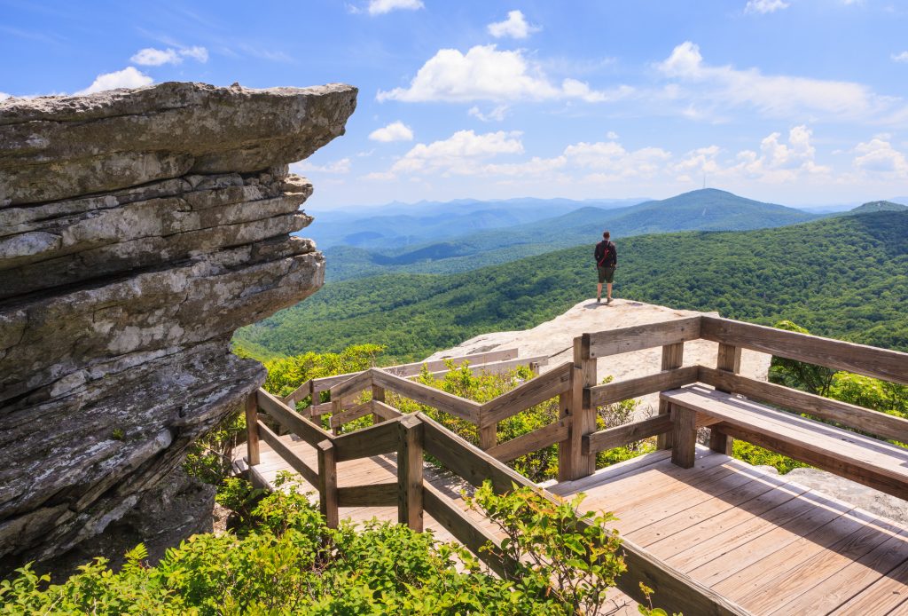 A hiker looks down at the forest below at the summit of Grandfather Mountain