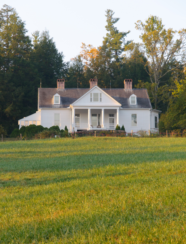 The exterior of the Carl Sandburg Home Historical Site, one of the best things to do in Asheville. It is an unassuming white farm house with a front porch and three chimney coming out of the roof. In front of the house is a large green lawn and behind it is a dense forest.