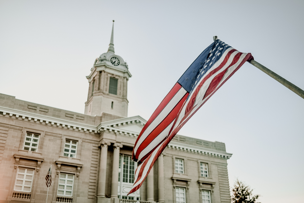 Looking up at a stone government building. It is a classic Greek Revival style building. There is a large American flag hanging in front of the building. One of the cutest small towns in Tennessee.