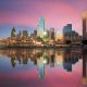 The Dallas skyline at twilight from the view of the river. The skyline is all lit up and the sky is mostly pink and purple with some blue. The sky and the skyline is reflected in the river. Best day trips from Dallas.