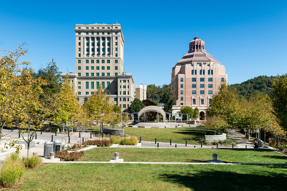 A view of downtown Asheville, one of the best places to see during a weekend in Asheville. There is a large green space, sidewalks, and old large buildings. 