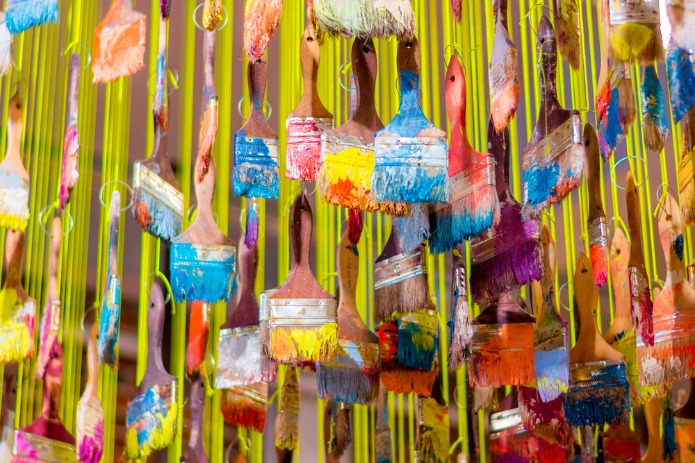 A close up of an art installation that is paintbrushes covered in various colors of paint hanging from yellow strings. 