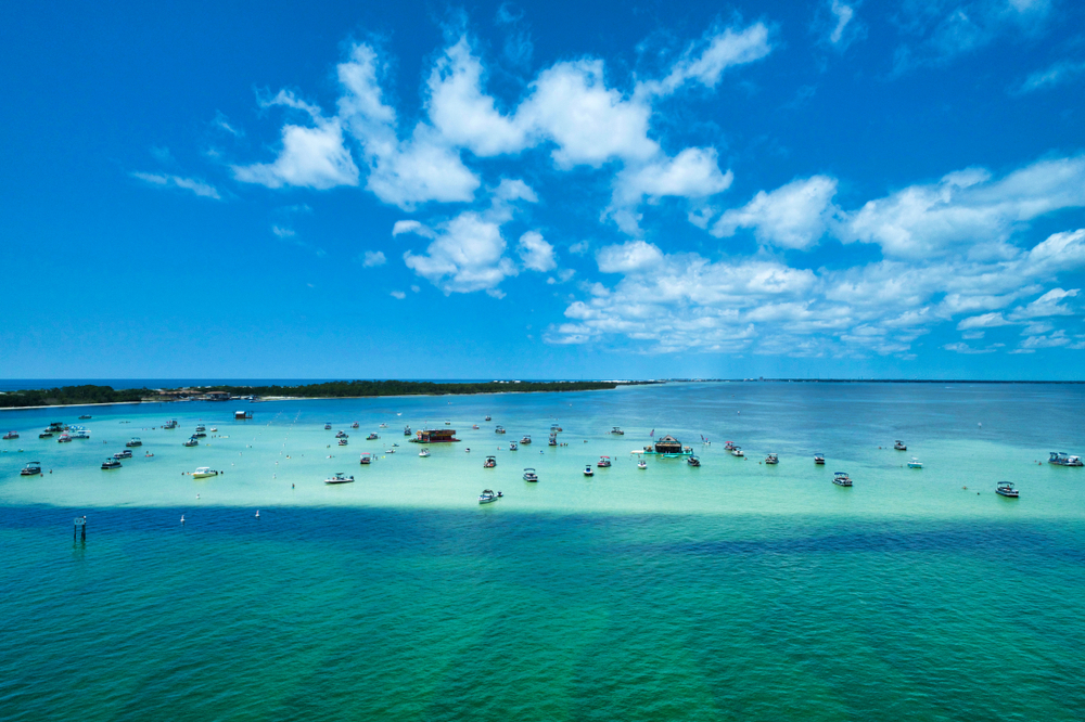 sand bar island with boats on top, different shades of blue water and bright blue sky