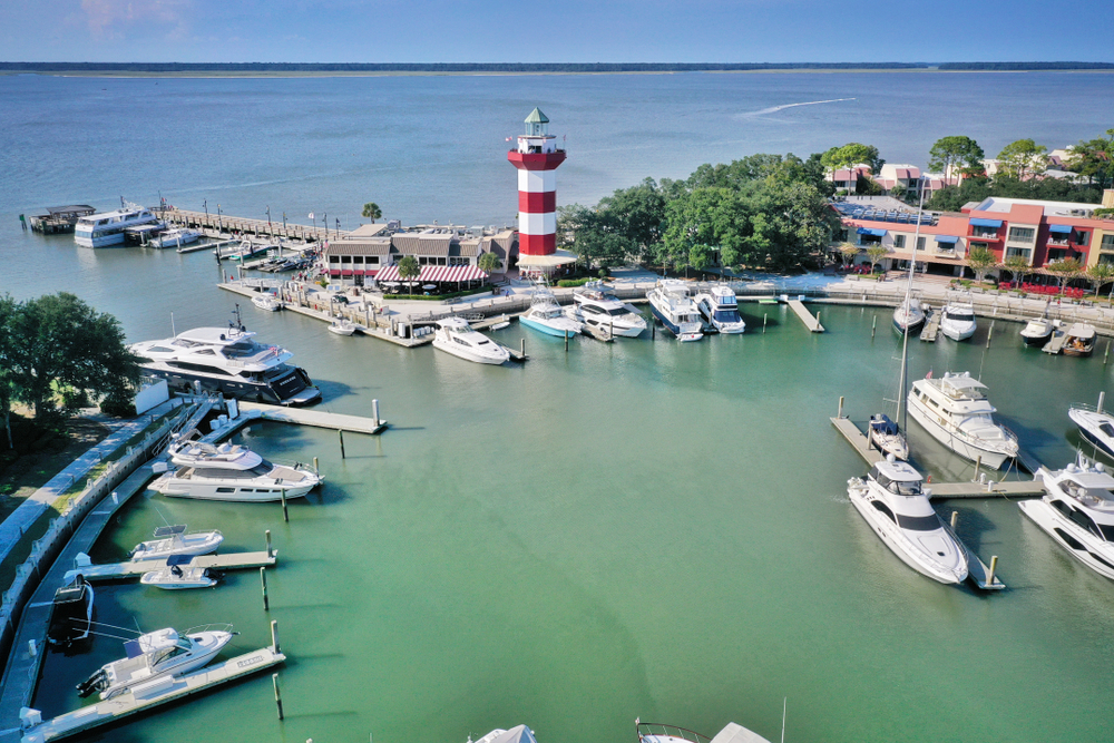 circular marina with boats parked inside, a red and white striped lighthouse by the water