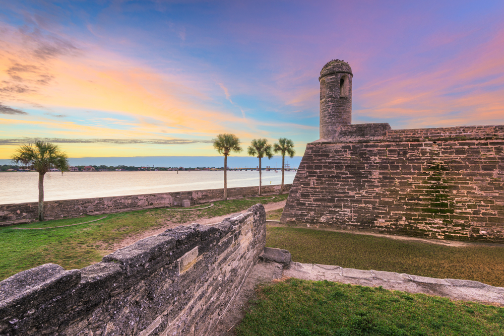 castle fort on waters edge, palm trees lining the water at sunset