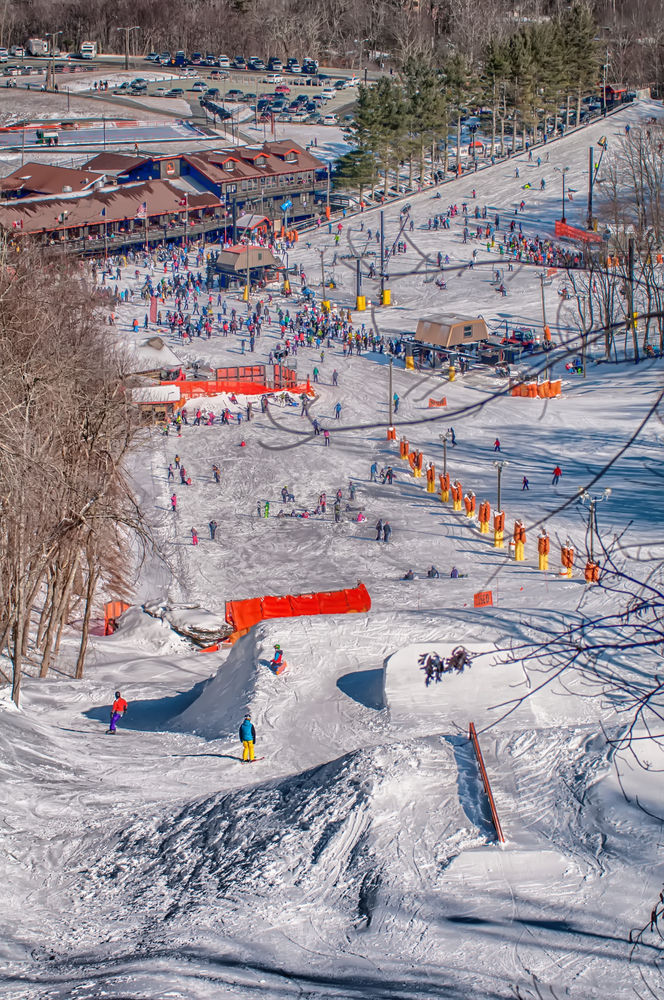 A picture of crowds of people skiing and snowboarding in various snowy sections of the Appalachian Mountain Ski Resort on a sunny day.