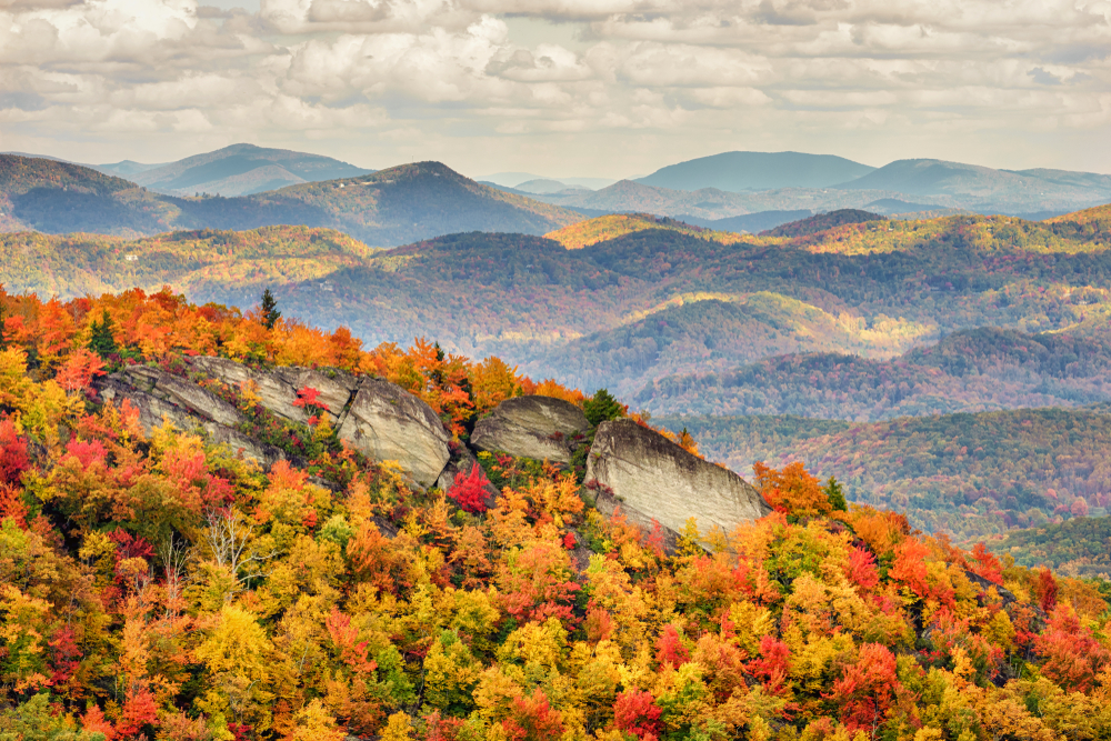 A photo taken from Grandfather Mountain that shows autumn trees covering the rolling mountains on a foggy day.