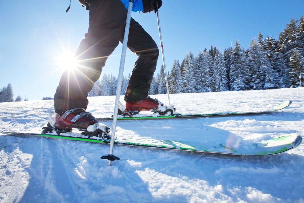 A picture of someone on skis and holding ski poles wit the sun shining behind them and over the snow covered ground.