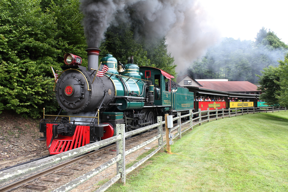 A picture of Tweetsie Railroad's steam train and the smoke bellowing from the front of it about to drive passengers away from the train station. 