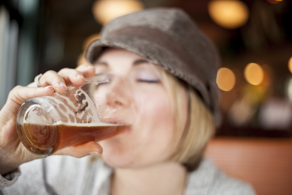 A woman in a hat drinking a pink of beer