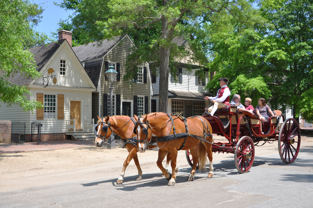 Horse drawn carriage with people riding in it passing by a house in Williamsburg.