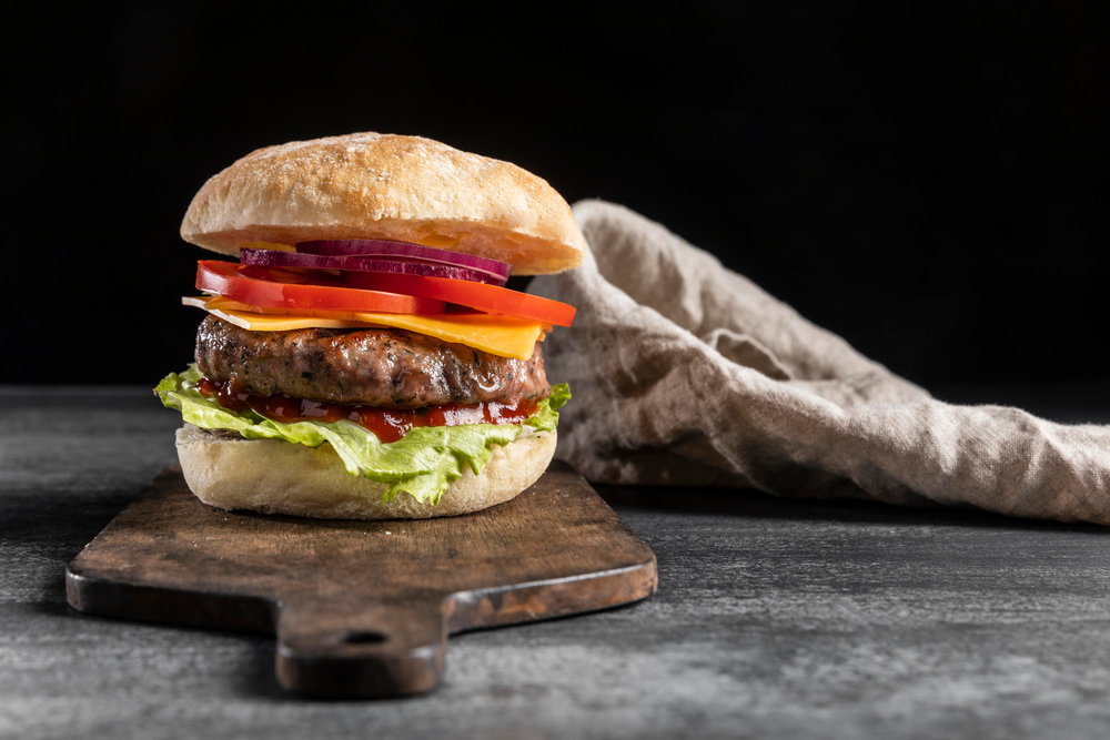 photo of a burger centered on a cutting board with a black background 
