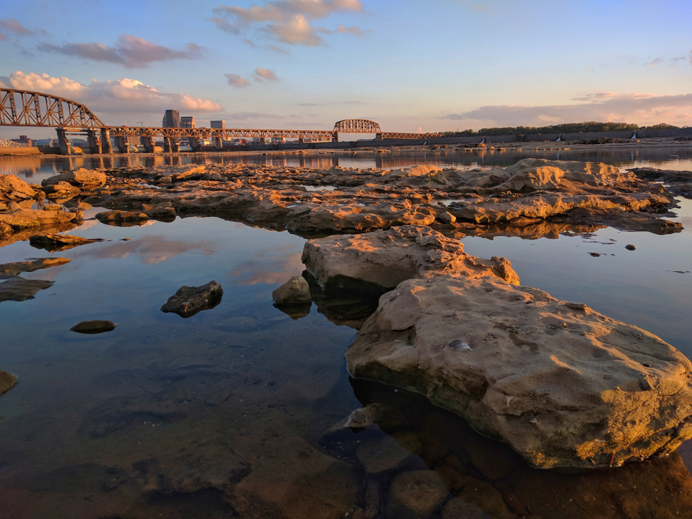 water in between rocks like little pools next to river with bridge in the background