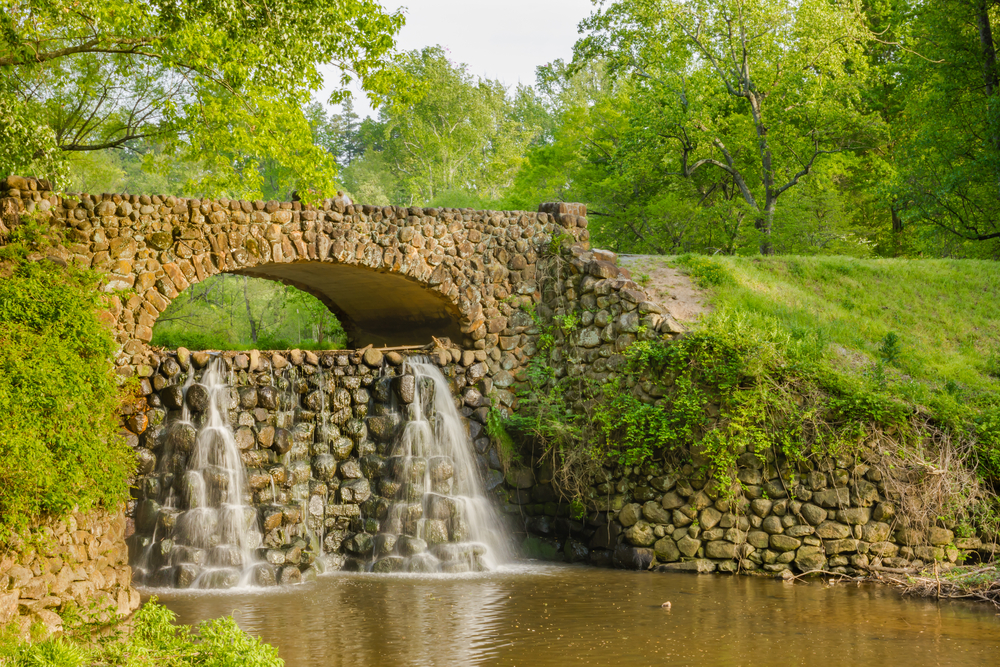 waterfall falling over mad made stone feature, surrounded by green trees and grass