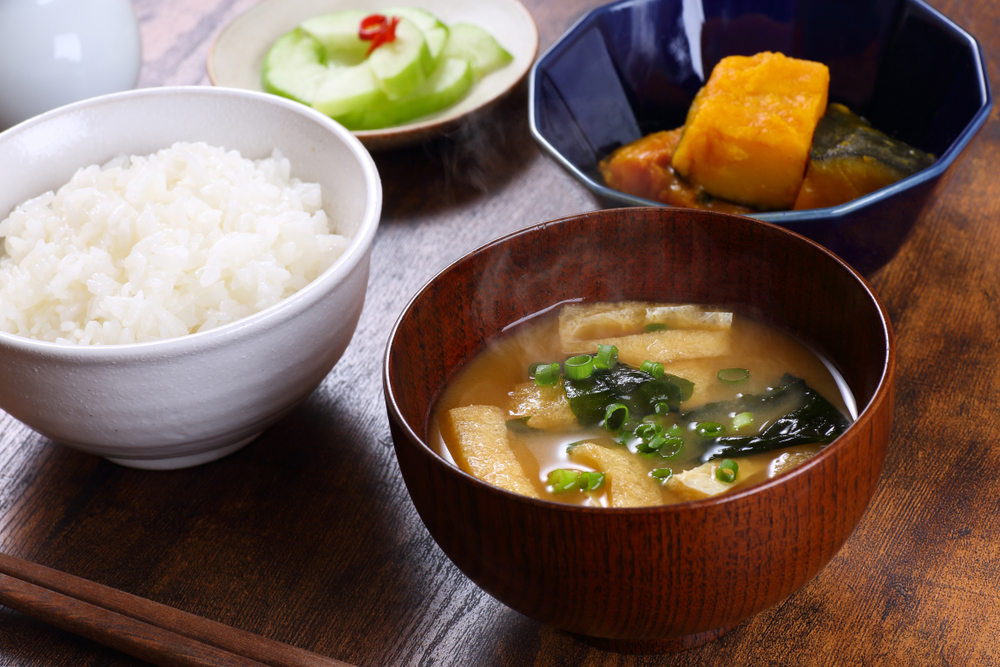 Miso soup, rice, and cucumbers served in separate bowls.