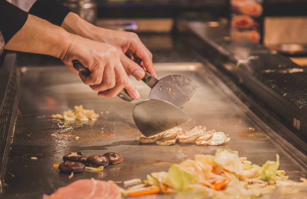 Hands cooking chicken on a hibachi stove representing Koi, one of the best restaurants in Augusta.