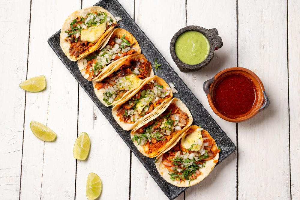 Aerial view of tacos with assorted sauces and limes.