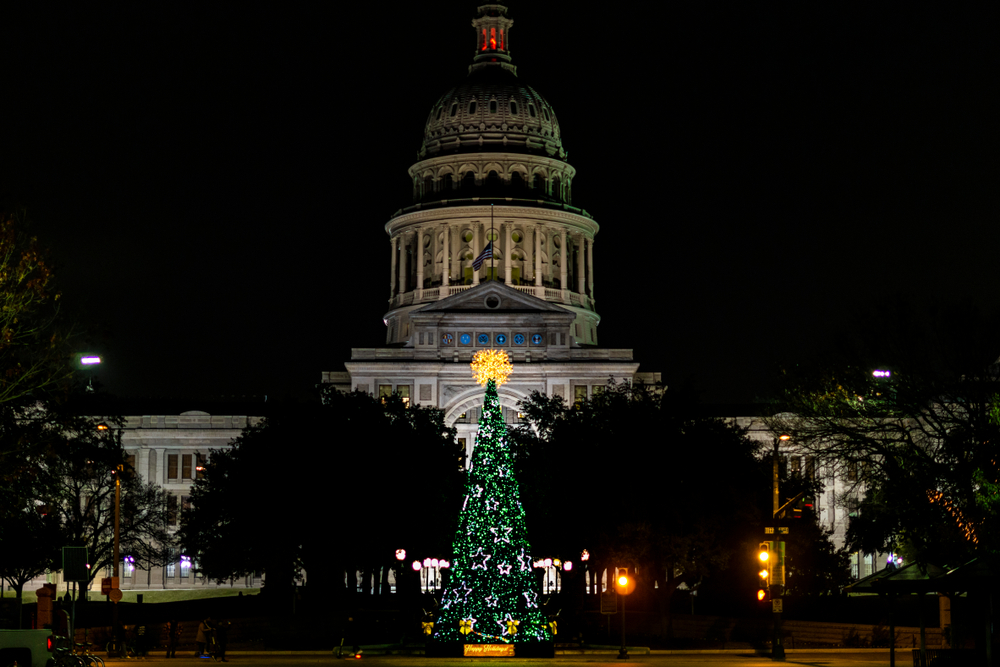 The Austin capital building in Texas at night. In front of it is a Christmas tree made of green lights with white stars and a big yellow orb of lights at the top. One of the best places to celebrate Christmas in the south. 