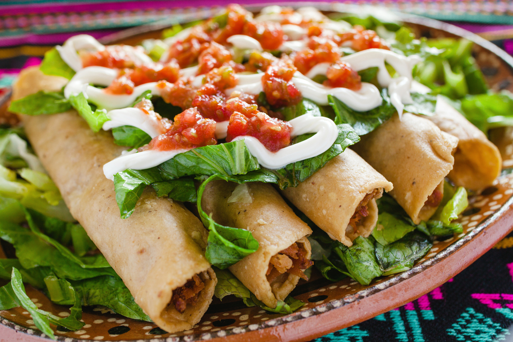 A plate of chicken flauta laying on a bed of lettuce. On top of the flautas is more lettuce, sour cream, and salsa. Mexican restaurants in Tupelo. 