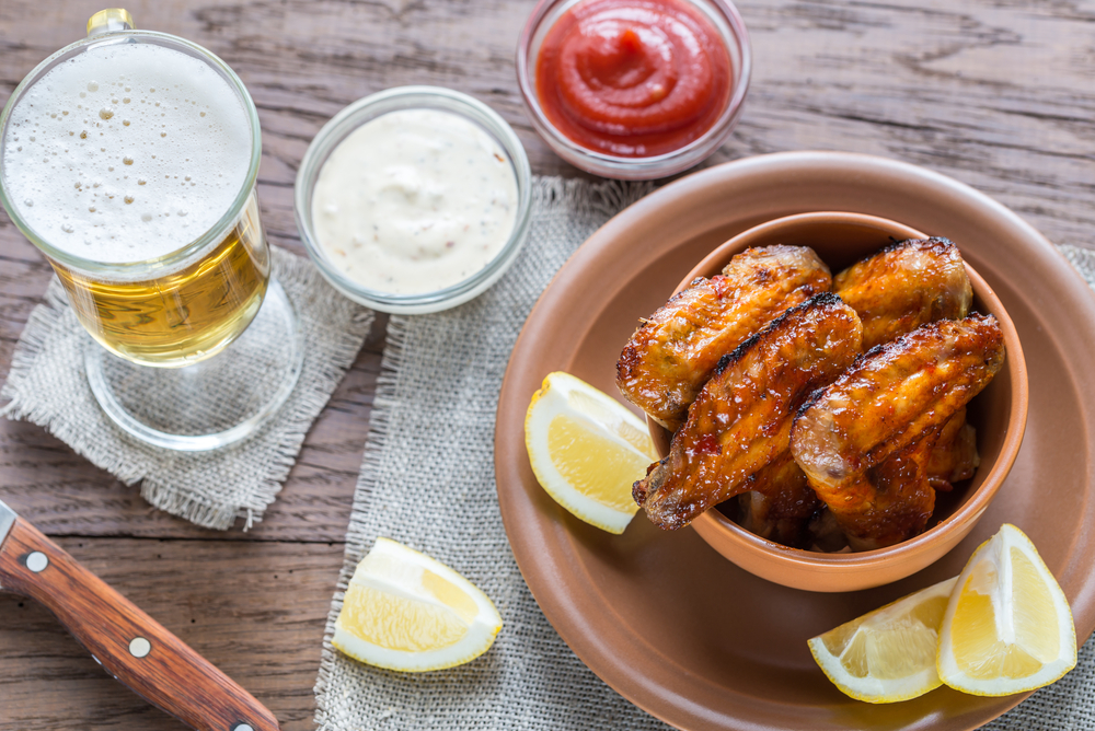 A bowl of fried chicken next to a beer and some ketchup, served with lemons.