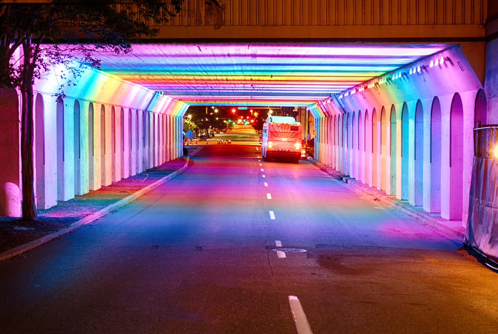 Undergroud bridge in Birmingham lit up in rainbow colors with a bus driving through.