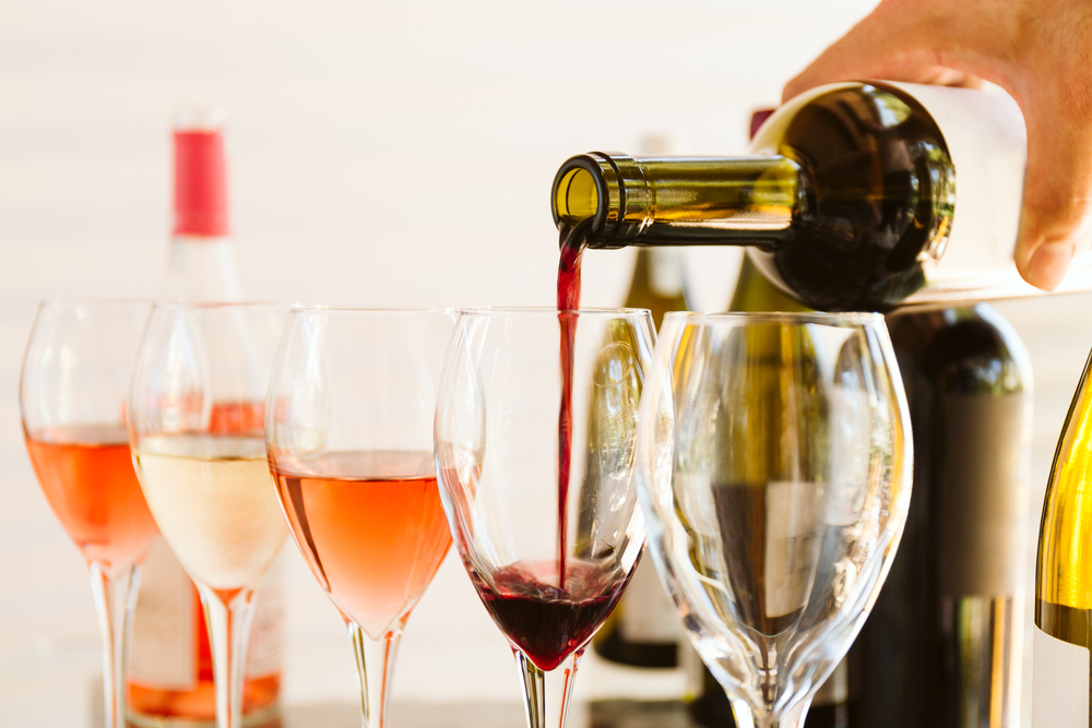 five wine glasses being filled with wine. White wine, rose wine, and red wine