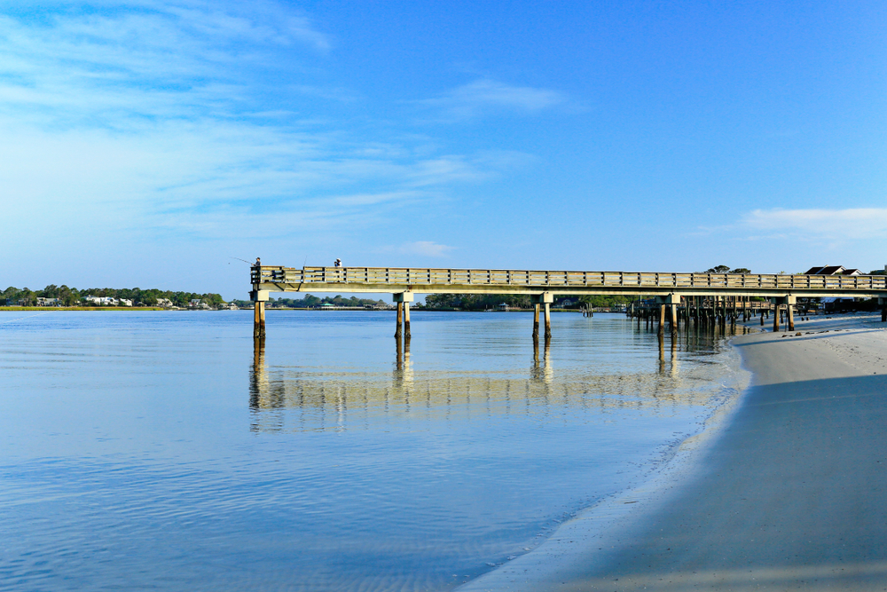 A fishing pier stretches into the water at Back River Beach, of the best river beaches in Georgia.