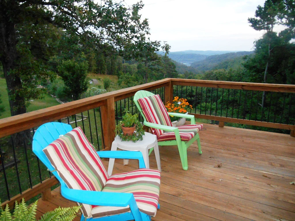 two chairs sitting out on the wooden deck of the cabin with views of the mountains and water in the distance