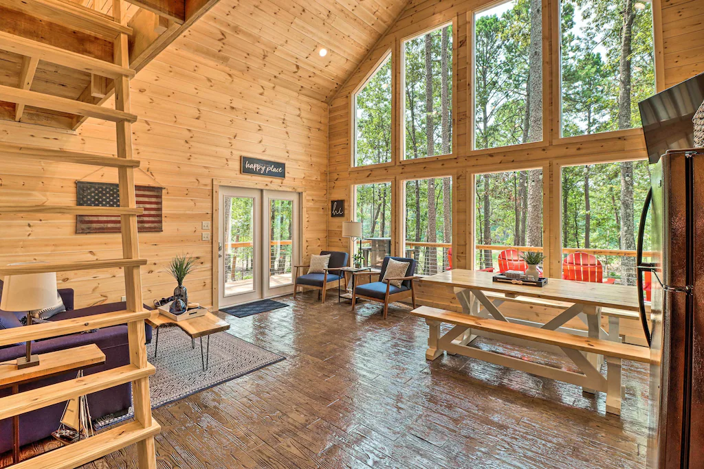 large windows from floor to ceiling in living area of one of the cabin in arkansas, picnic table style table and couch inside