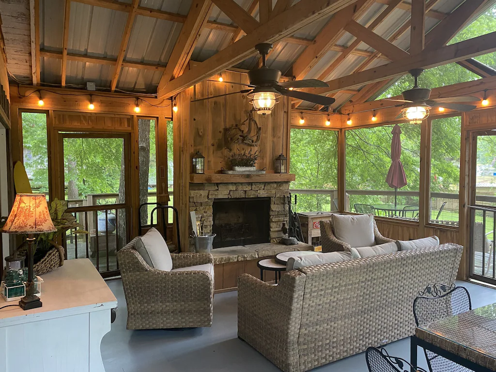 large screened in porch with furniture, lamps, string lights, fireplace, and tree views