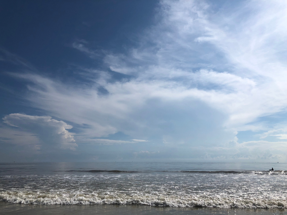Clouds above the horizon, with waves hitting the sandy shore on a sunny day at North Beach on Tybee Island in GA.
