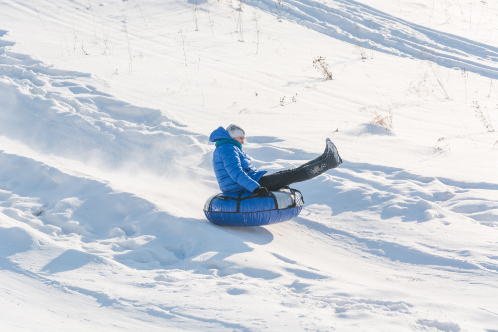 Snow tubing, one of the best things to do during Christmas in Tennessee. A man in a coat, boots, and hat is sliding down a hill of snow tube.