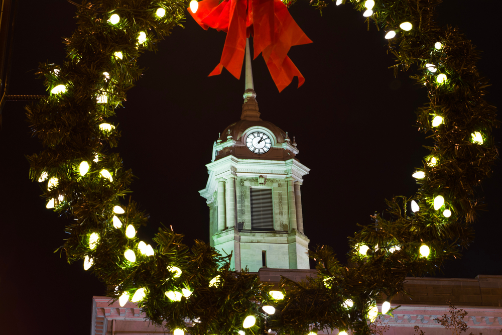 view of a clock tower through a wreath that has lights and a bow on it