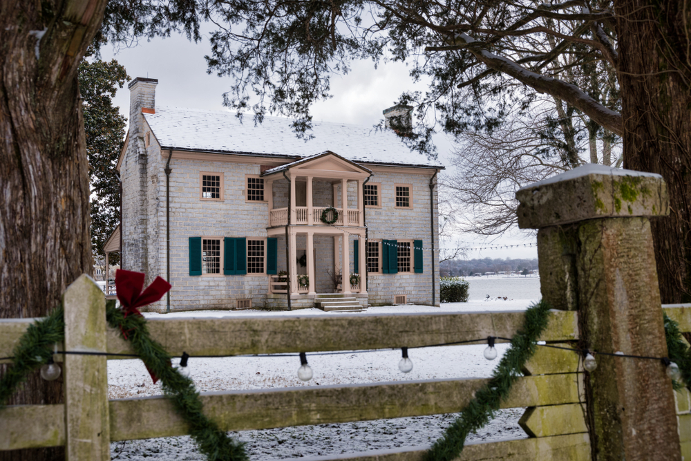 Rock home that is two stories. Both the home and the fence in front of the home are decorated for the holiday with garland, bows, and wreaths