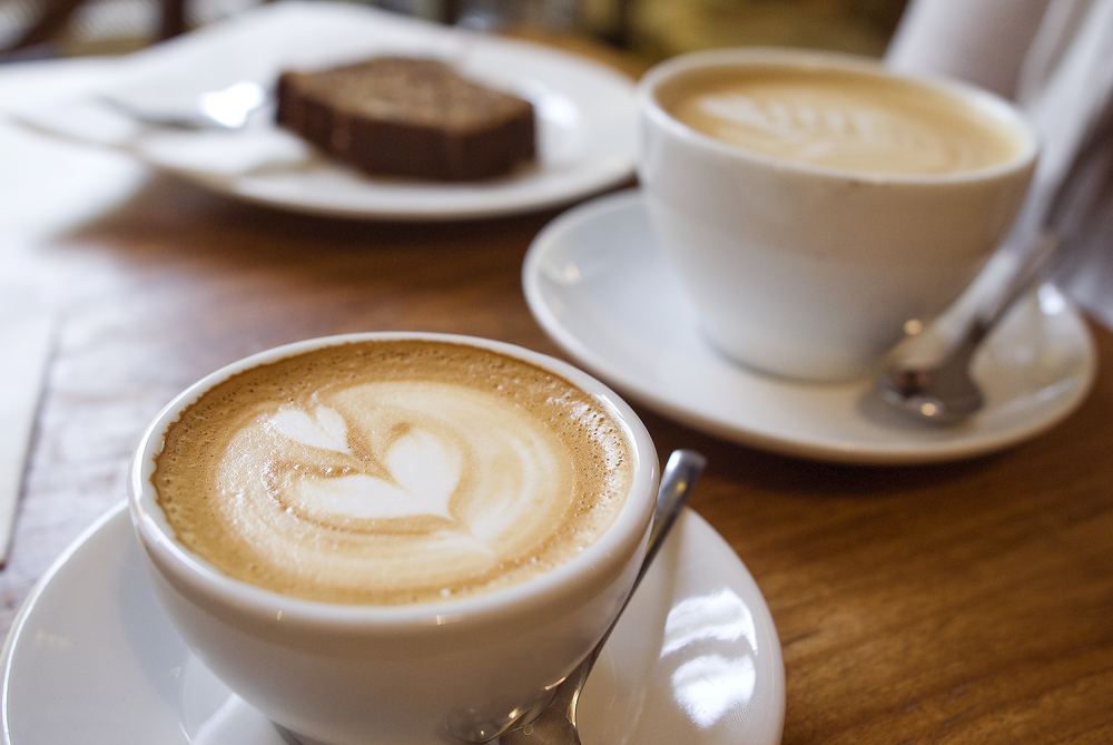 Two coffee cups on the table with a slice of cake.