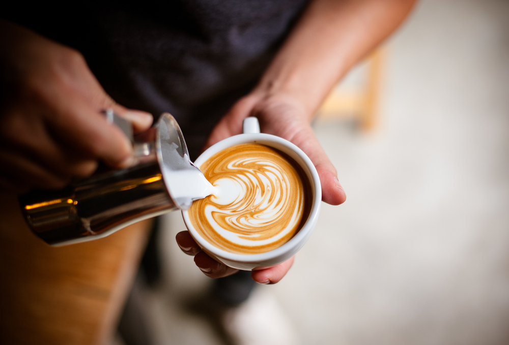 A barista pouring the milk into a latte cup