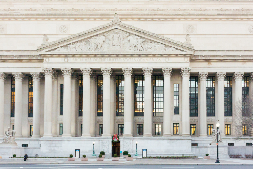 The exterior of the National Archives Museum. It is a large Greek revival style building that has large Roman columns and intricate carvings. 