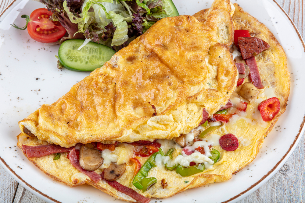 a stuffed breakfast omelette on a plate with a small salad