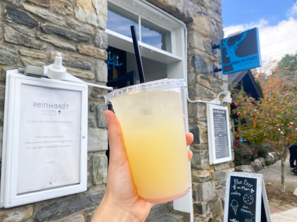 A hand holding a refreshing glass of lemonade in front of Blue Door on Main