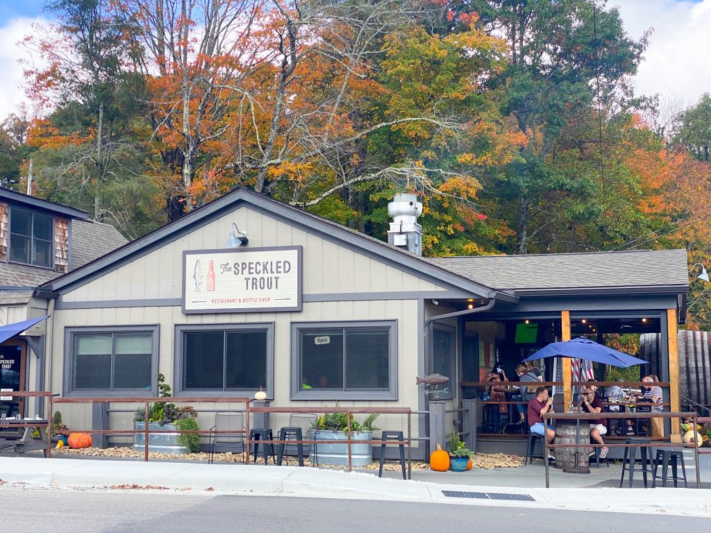 The outside of the Speckled Trout restaurant with outdoor seating area and fall trees int he background
