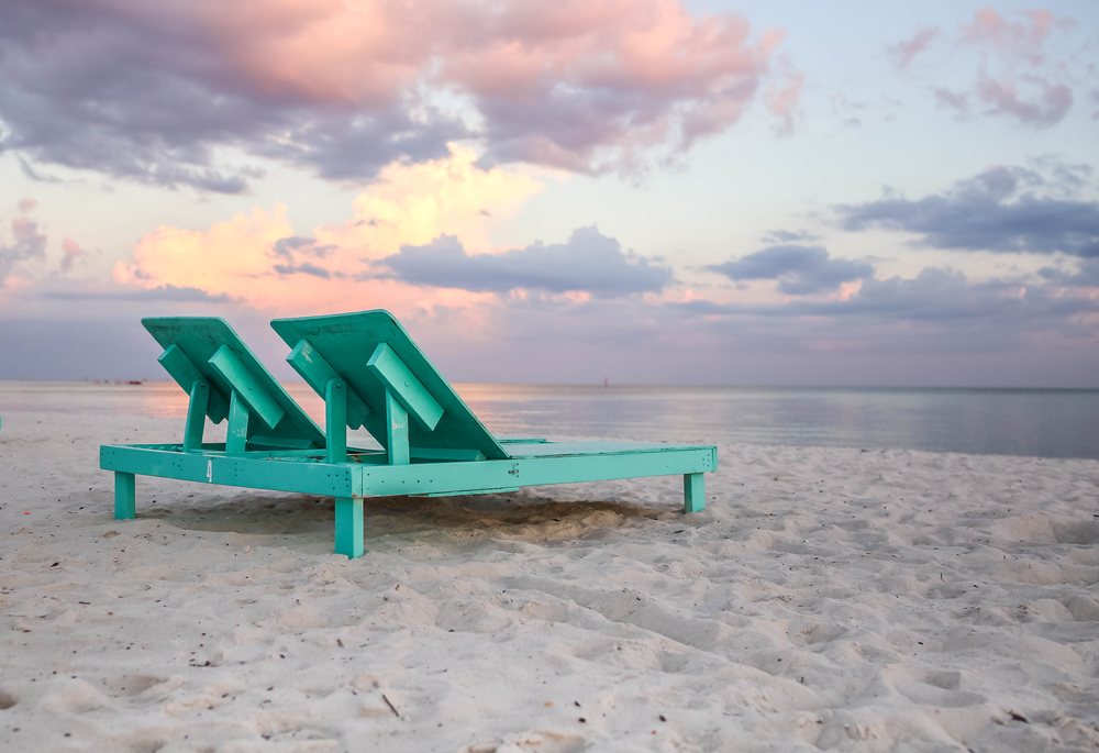 Sunset at Biloxi Beach with a light green, wooden lounge chair.