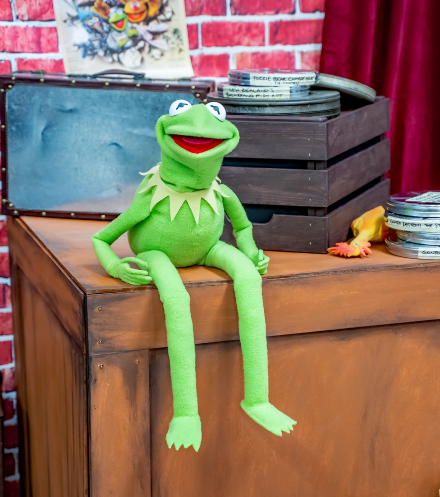 Kermit the Frog sitting on a desk with a crate full of film reels.