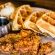 Seasoned chicken and Belgian waffle wedges on a plate with a container of maple syrup, similar to the dish served at one of the best restaurants in Boone, NC.