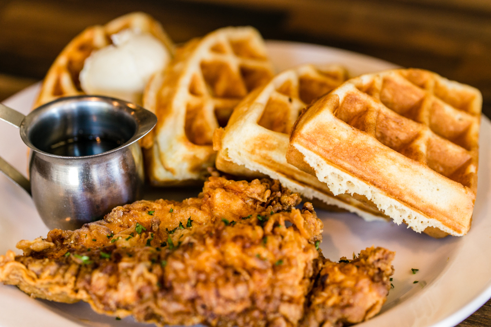 Seasoned chicken and Belgian waffle wedges on a plate with a container of maple syrup, similar to the dish served at one of the best restaurants in Boone, NC.