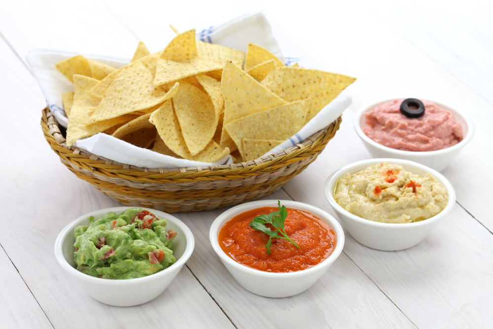A basket of corn tortilla chips with four different dips in varying color and consistency, similar to the chips served at Dos Amigos, one of the Mexican restaurants in Boone, NC.