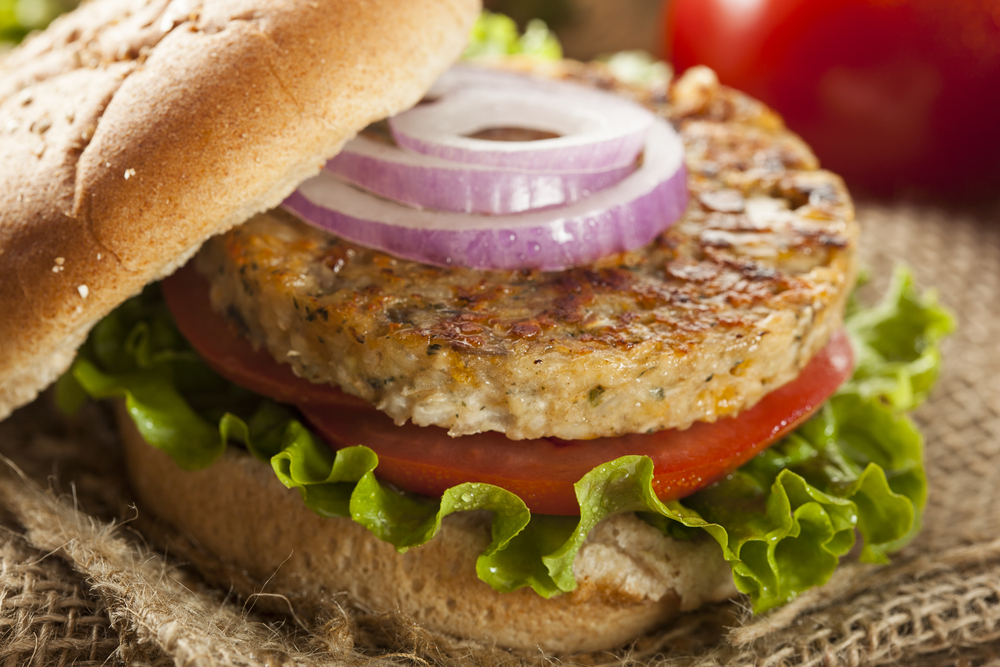 A veggie burger sits on a burger bun with lettuce, tomato, and onion, similar to the veggie burgers you can order from Wild Craft Eatery in Boone, NC.