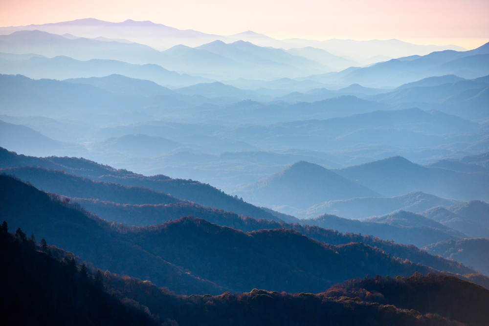 The Blue Ridge Mountains in North Carolina. You can see mountain peaks and ridges for miles. The sun is setting so the mountains look blue. 